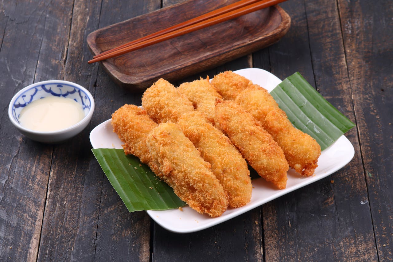 Crispy fried banana fritters served on a plate with creamy dipping sauce, perfect for a tropical treat.